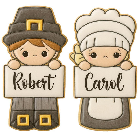 Decorated sugar cookies shaped like pilgrim boy and pilgrim girl characters holding blank signs for personalization. Each cookie is decorated witth traditional pilgrim outfits including bonnets and hats. Example names written on the cookies make them perfect as edible place cards, personalized Thanksgiving treats, and fall holiday cookie cutters.