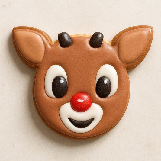 A decorated cookie shaped like a reindeer&#39;s face with a red nose, black eyes, and a smiling mouth, on a light-colored surface.