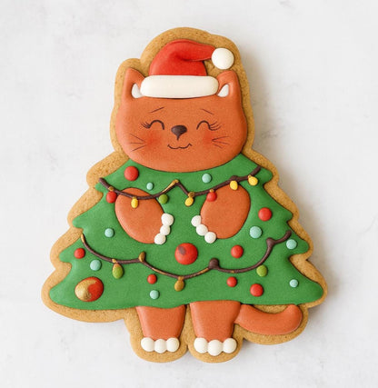 A festive cat-shaped cookie designed as a Christmas tree. The cat wears a red Santa hat and green tree outfit decorated with colorful Christmas lights and ornaments. Its paws and face are detailed with brown icing and a happy smile, giving it a cozy holiday charm.