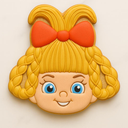A cookie shaped like a smiling blonde girl with big blue eyes, braided hair, and a large red bow on top. The design captures a cheerful Whoville-style character, evoking festive holiday charm and classic Christmas nostalgia.