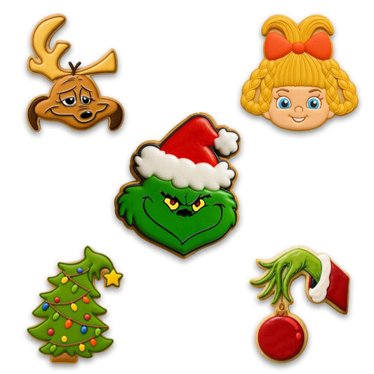 A festive cookie set inspired by The Grinch, including cookies shaped like the Grinch in a Santa hat, Max the dog with an antler, a Who girl with blonde braids and red bow, a crooked green Christmas tree with lights, and the Grinch’s green hand holding a red ornament.