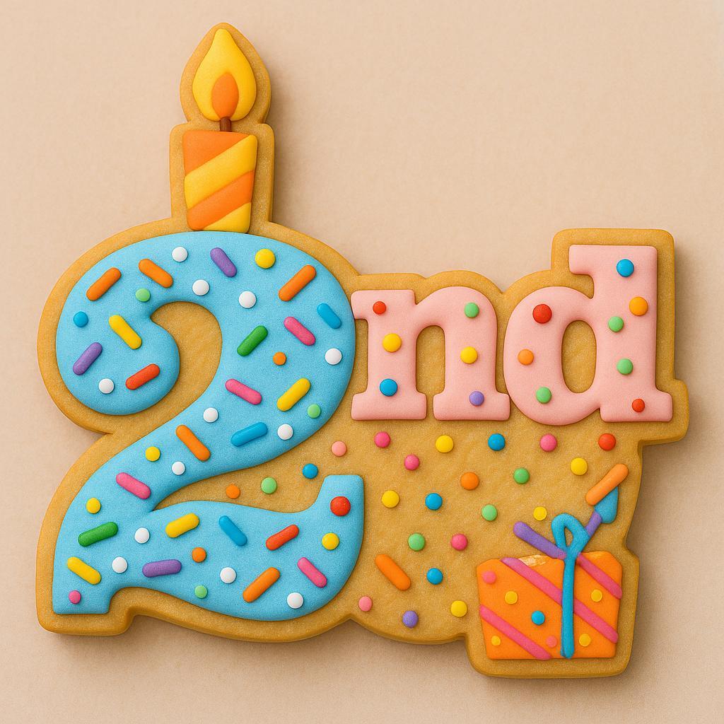 A festive sugar cookie shaped like the phrase “2nd,” featuring a blue number two decorated with colorful sprinkles and a candle flame on top, the letters “nd” in pink, and a small orange present with blue ribbon at the bottom right.