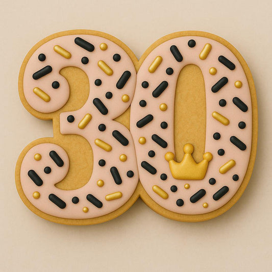 A sugar cookie shaped like the number 30, decorated with blush pink icing covered in gold and black sprinkles, and a small gold crown detail on the zero.