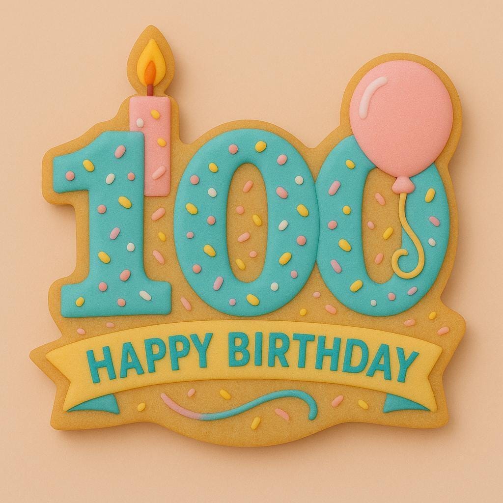 A sugar cookie shaped like the number 100, decorated with blue icing and pastel sprinkles. The number 1 has a pink candle on top, and one of the zeros has a pink balloon attached. A yellow banner across the bottom reads “HAPPY BIRTHDAY.”