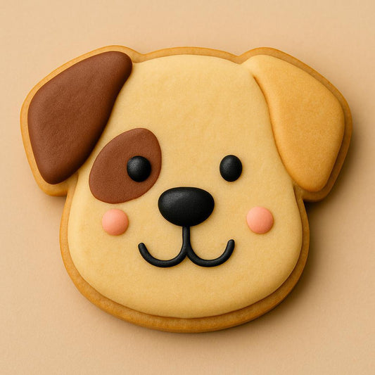 A sugar cookie shaped like a puppy’s head, decorated with tan and brown icing, pink cheeks, a black nose, and a happy smile.