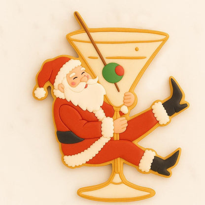 Decorated sugar cookie of Santa Claus sitting inside a martini glass with an olive garnish, surrounded by gold stars on a white background.