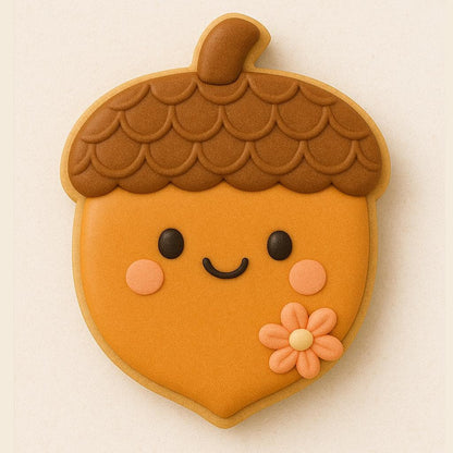 An acorn-shaped cookie with a smiling face and a flower. The top of the cookie is brown with a tetured pattern, while the botton is orange. The cookie has black eyes, pink cheeks, and a curved black mouth. A small, orange flower is on the bottom right. Perfect for class room treats or Thanksgiving Harvest platters.