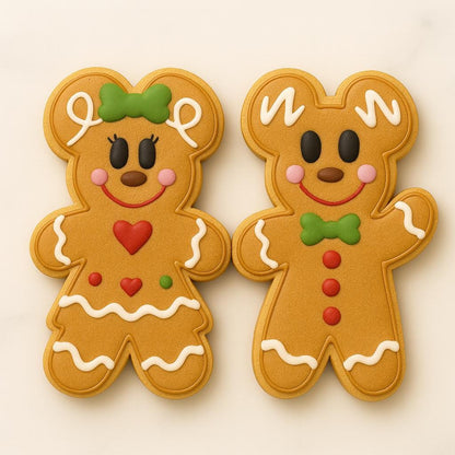 A matching set of two gingerbread cookies — one styled as a girl with a green bow, red heart, and icing skirt trim, and one styled as a boy with a green bow tie and red buttons. Both have smiling faces, pink cheeks, and white icing details, creating a festive and adorable holiday pair.