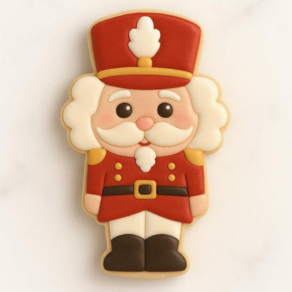 A cookie shaped like a toy soldier Santa wearing a red uniform with gold buttons and a tall red hat. The design features a smiling face with a white mustache, rosy cheeks, and black boots, capturing a cheerful nutcracker-style holiday look.