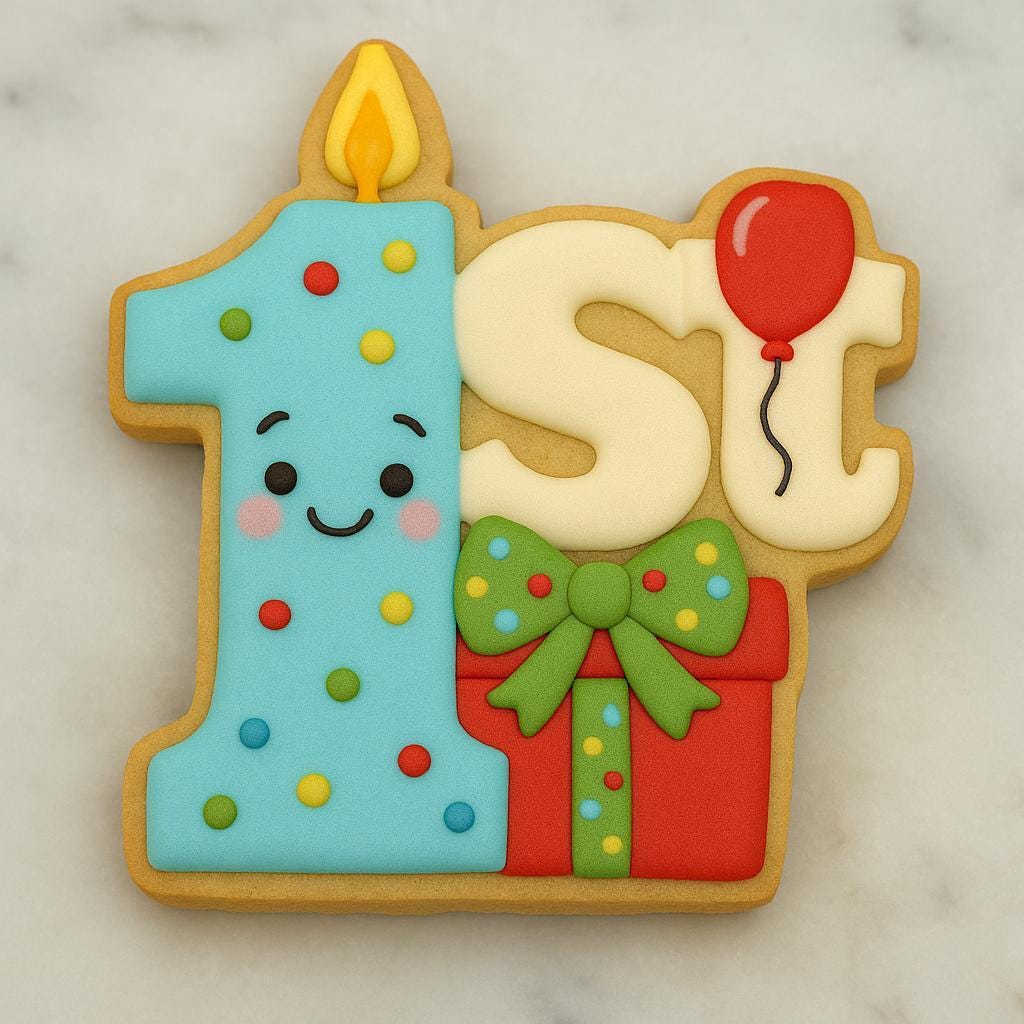 A colorful sugar cookie shaped like the phrase “1st,” with a light blue number one decorated with confetti dots and a smiling face, a yellow flame on top, a white “st” with a red balloon, and a red gift box with a green polka-dot bow at the bottom.