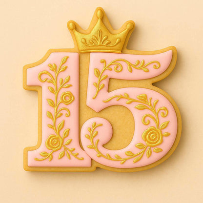 A pink sugar cookie shaped like the number 15 with intricate gold floral designs and a golden crown on top, representing a quinceañera or 15th birthday celebration.