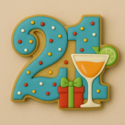 A sugar cookie shaped like the number 21, decorated with bright blue icing covered in colorful sprinkles, featuring a cocktail glass with an orange drink and lime garnish, and a red gift box with a green bow.