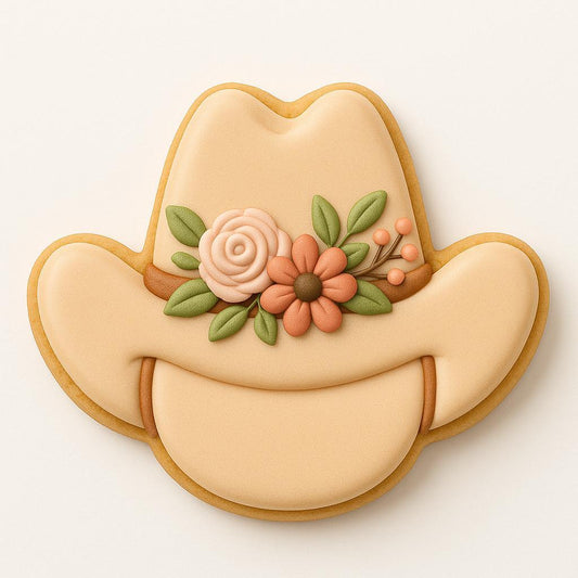 A sugar cookie shaped like a cowboy hat, decorated in beige icing with a floral cluster of peach and cream flowers, green leaves, and soft orange berries across the band.
