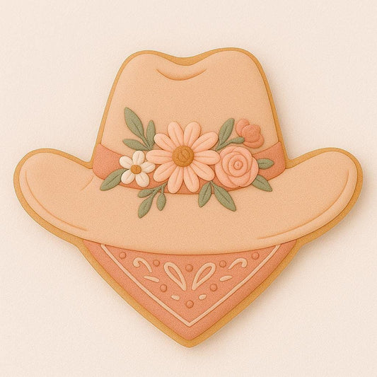 A sugar cookie shaped like a wide-brimmed cowboy hat with a floral crown of peach, cream, and sage flowers, resting above a paisley bandana in soft terracotta tones.