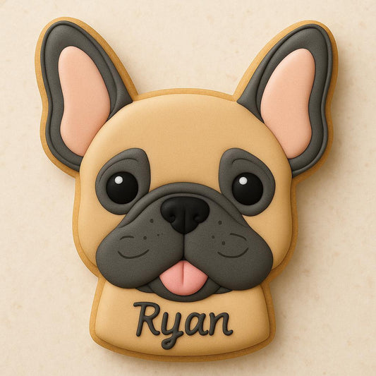 A sugar cookie shaped like a French Bulldog’s head, decorated with tan and gray icing, black eyes, a pink tongue, and the name “Ryan” written at the bottom.