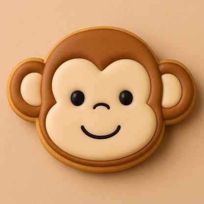 A sugar cookie shaped like a monkey’s head, decorated with tan and brown icing, black eyes, and a smiling mouth on a warm beige background.