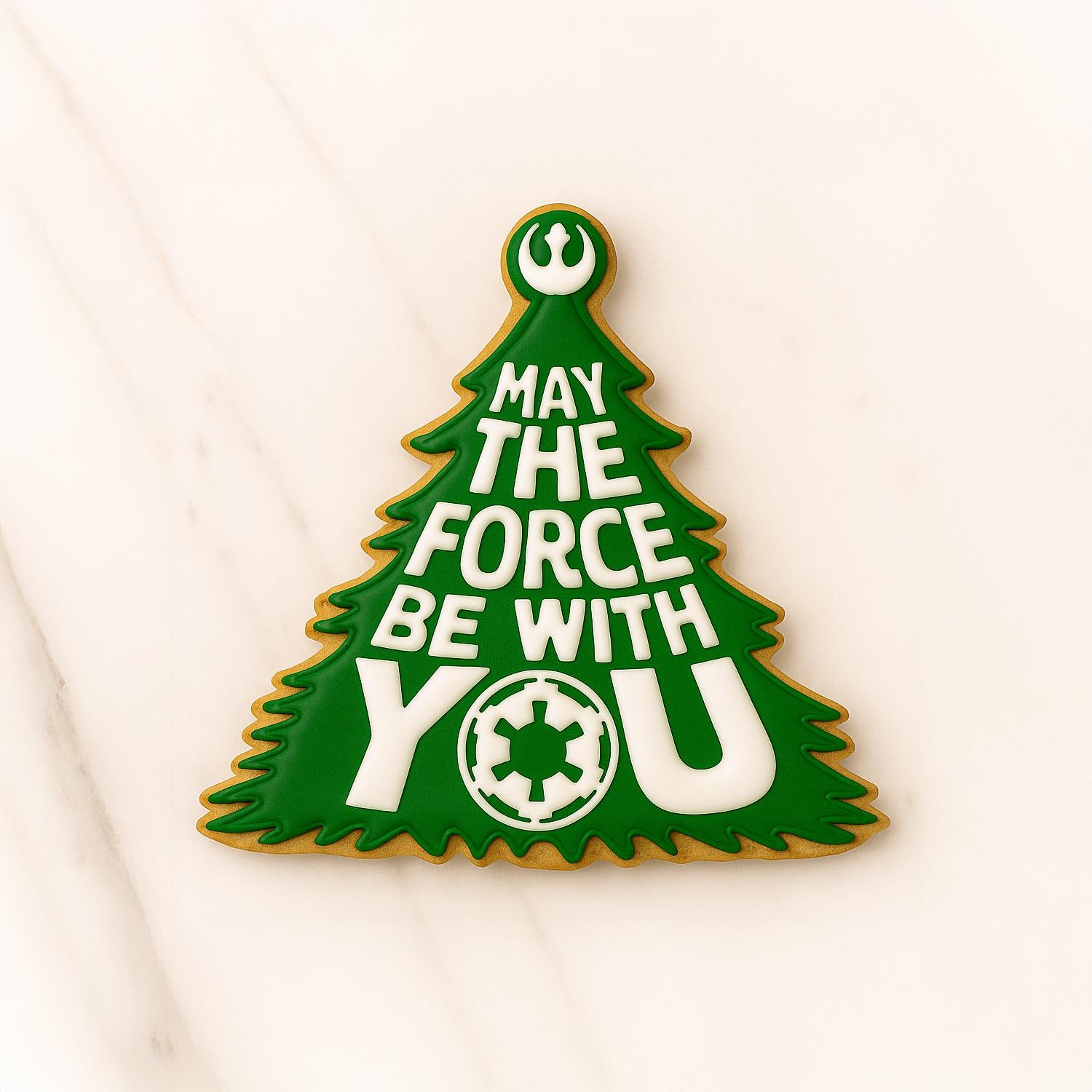 Decorated sugar cookie shaped like a green Christmas tree with the text “May the Force Be With You” in white icing, featuring Star Wars symbols, on a marble background.