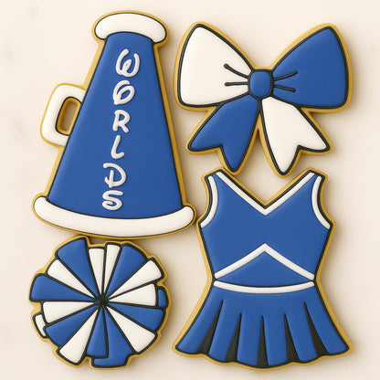 Decorated sugar cookies shaped like cheerleading items — a blue megaphone with “Worlds,” a blue and white bow, a pom-pom, and a cheer uniform — arranged on a neutral background.
