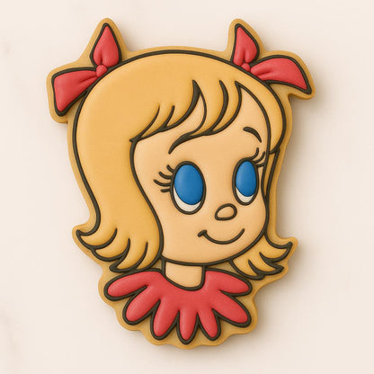 Decorated sugar cookie shaped like Cindy Lou Who with blonde hair, blue eyes, red bows, and a red collar, on a light marble background.